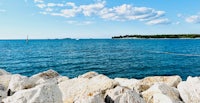 a view of the ocean with rocks and a sailboat