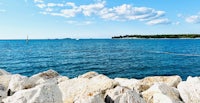 a view of the ocean with rocks and a sailboat