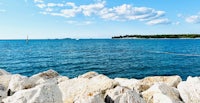 a view of the ocean with rocks and a sailboat