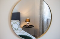 a round mirror in a bedroom with a bed and nightstand